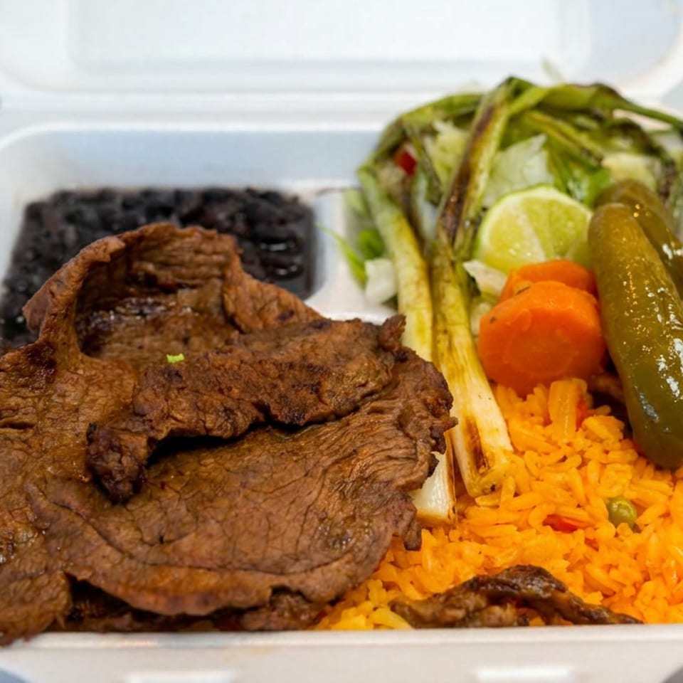 Takeout container filled with grilled steak, black beans, orange rice, salad, lime, tomato, and a whole pickled jalapeño.
